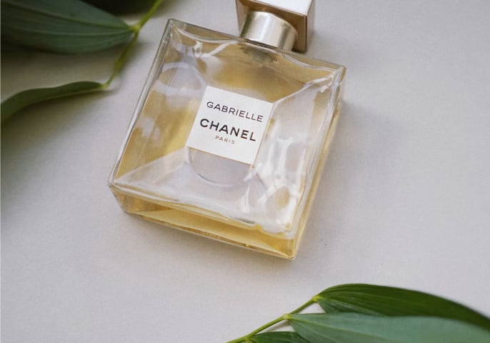 Perfume Bottle laying on a white table with leaves above and below it.